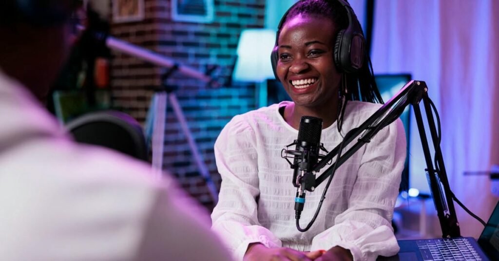 How To Get on Podcasts As a Guest? – Tips to Land Your Spot Person speaking into a microphone with headphones in a podcast studio with brick wall and colorful lights.