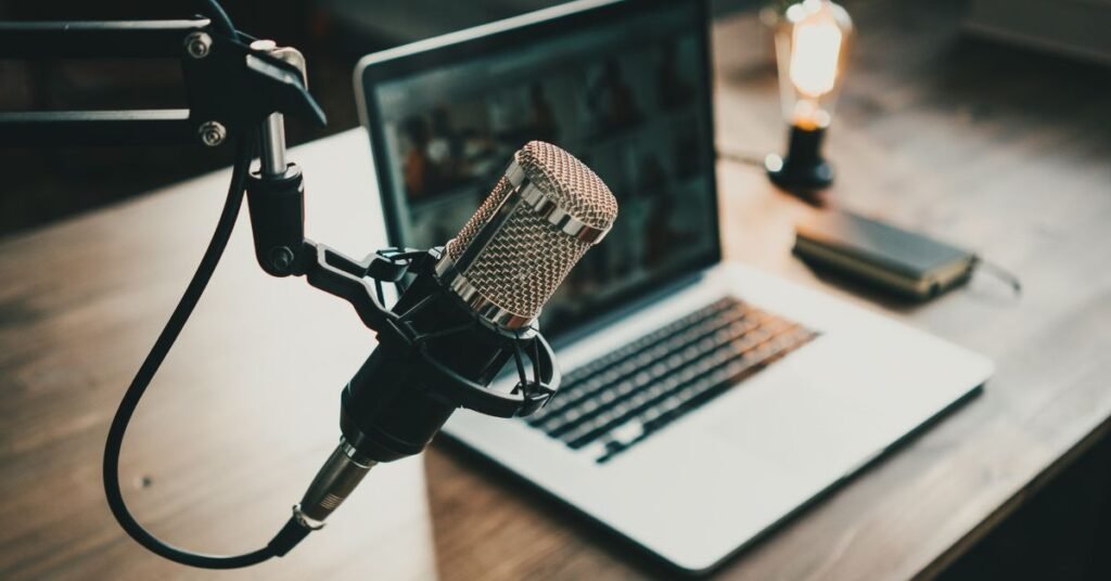 Why Are Podcasts So Popular? Exploring Their Worldwide Rise Podcast setup with microphone, laptop, and lamp on a wooden desk.