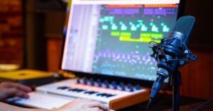 Music production studio with a microphone on a stand, MIDI keyboard, and laptop displaying audio editing software.