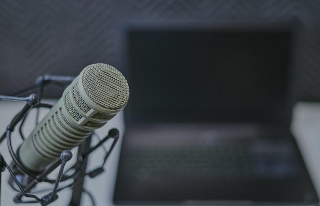 How To Cite a Podcast MLA? – Step-by-Step Guide Condenser microphone in podcast setup with laptop and dark patterned background.