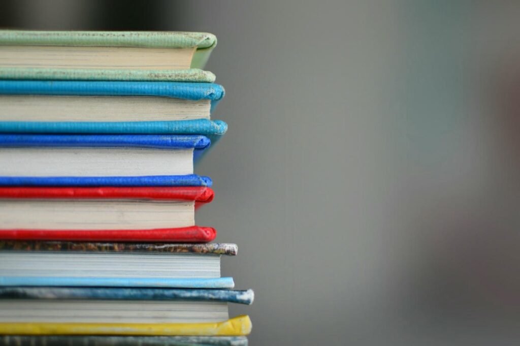 24 Best Educational Podcasts to Boost Your Knowledge Vibrant stack of books with green, blue, red, and yellow covers on a blurred gray background.